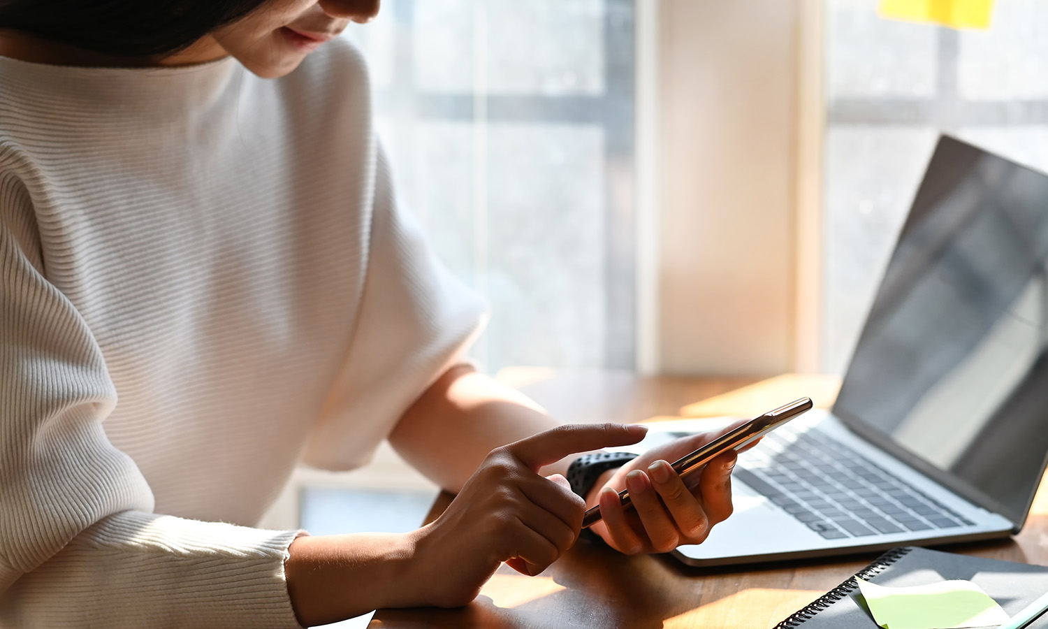 Close up of woman looking at her phone with laptop nearby